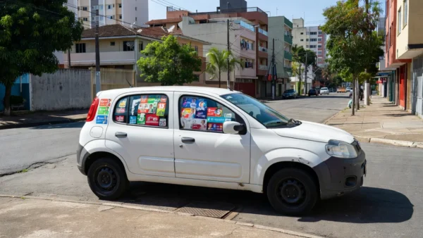 Carro com adesivos eleitorais para eleições 2026 em rua brasileira, aviso para seguradora